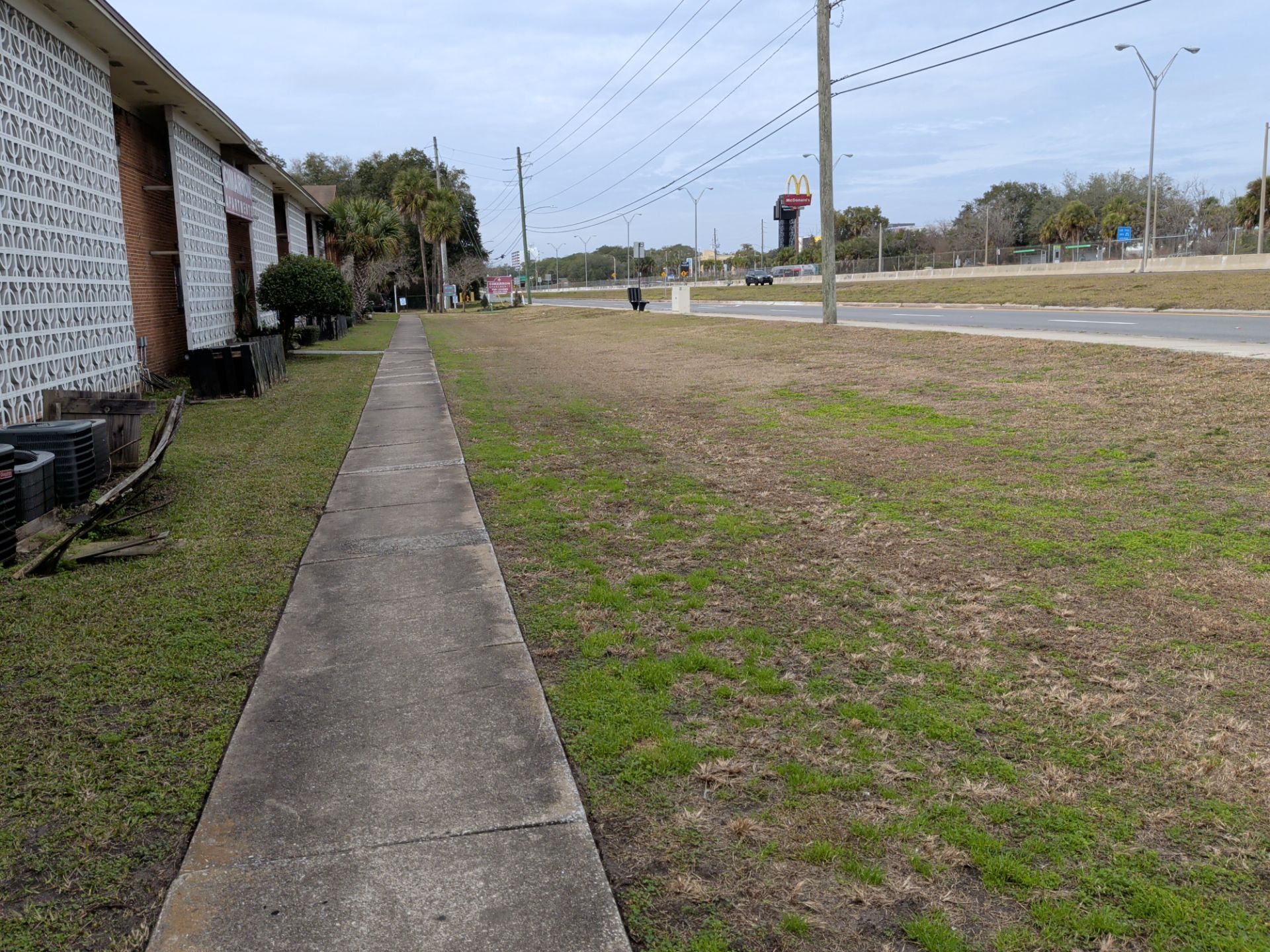 Sidewalk next to a building, leads to a road with a water tower visible.
