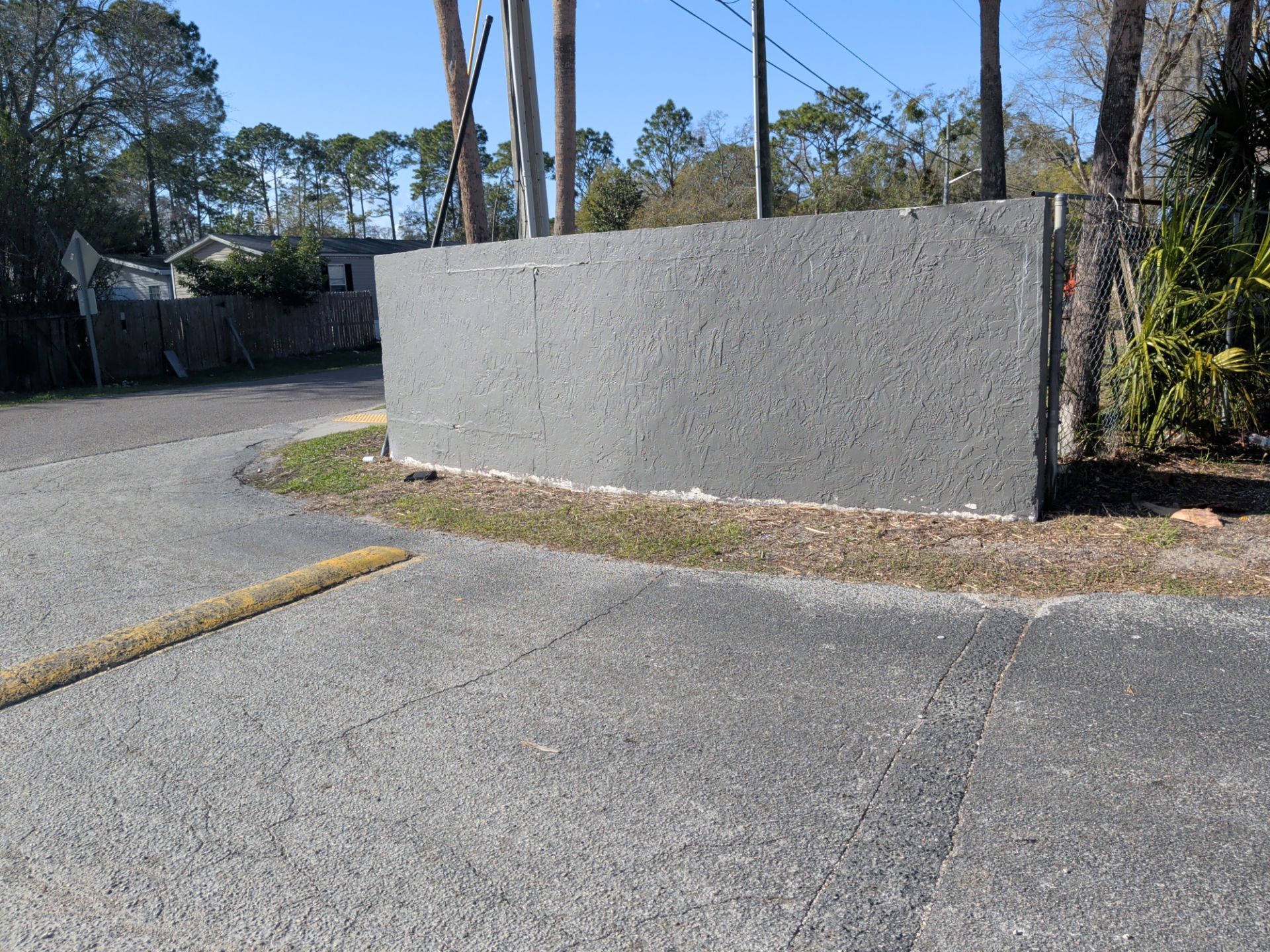 Concrete wall beside a paved road in a quiet outdoor area with trees and utility poles