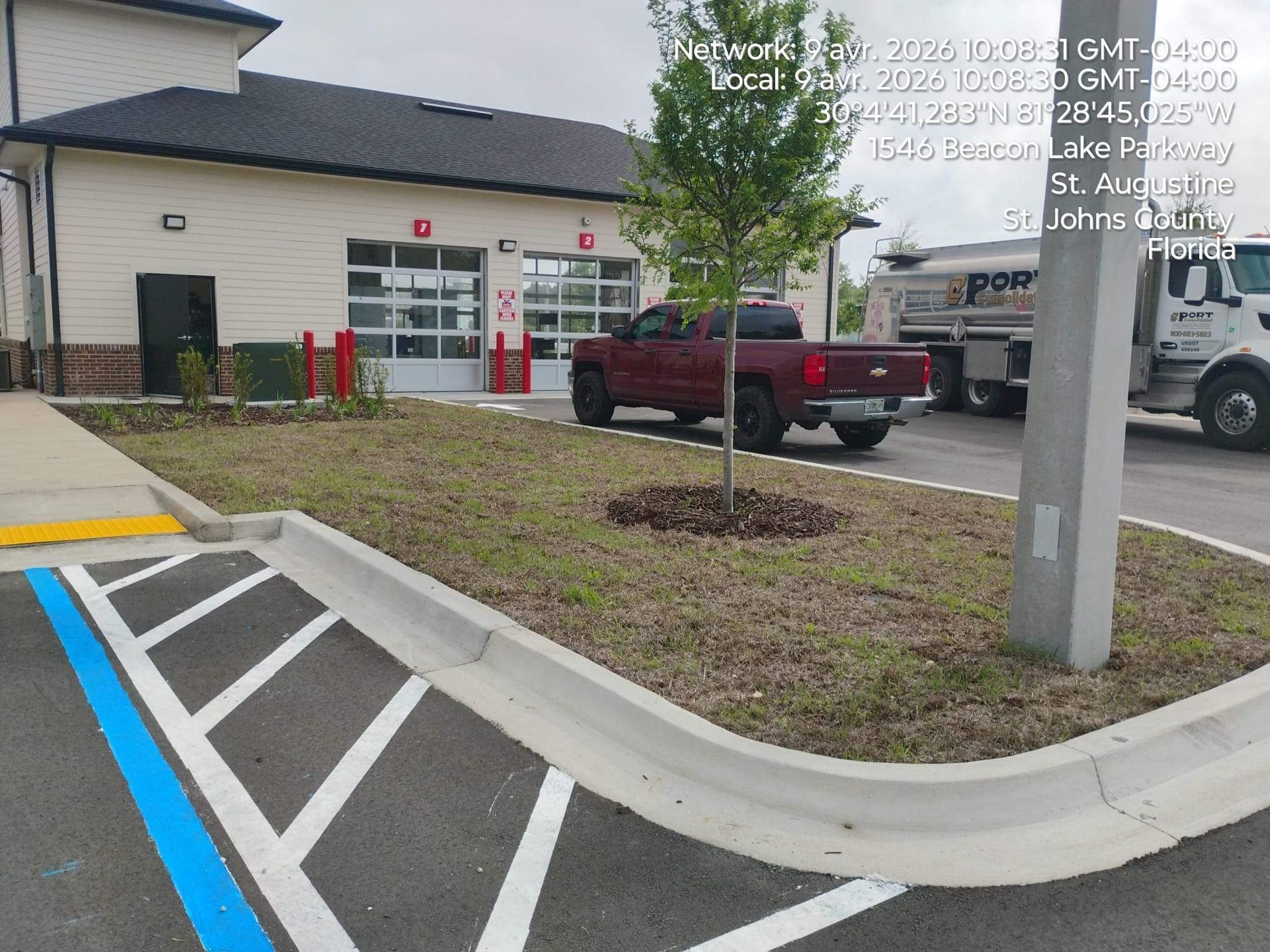 Parking lot curb ramp with blue handicap striping, red pickup truck, and building entrance in background