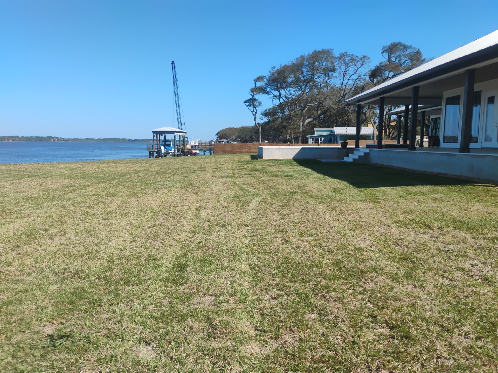 Grassy waterfront lawn beside a building, with a blue sky and water in the background