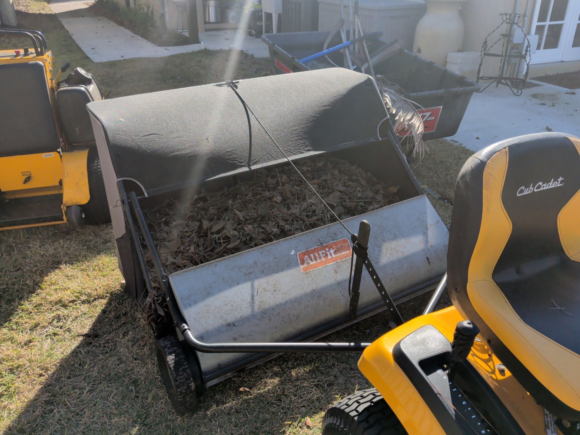Yellow riding mower with attached grass sweeper parked on a lawn near a house.