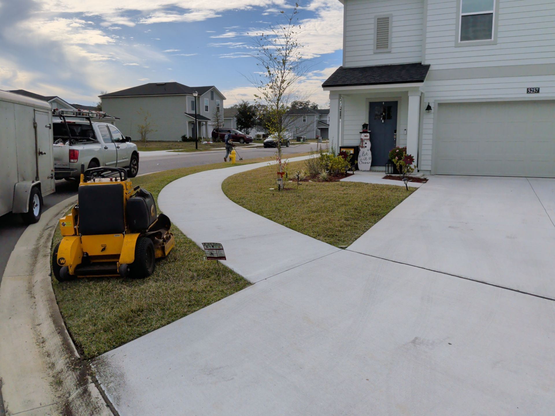 Newly paved curved sidewalk beside a suburban house with a yellow lawn mower and parked work van