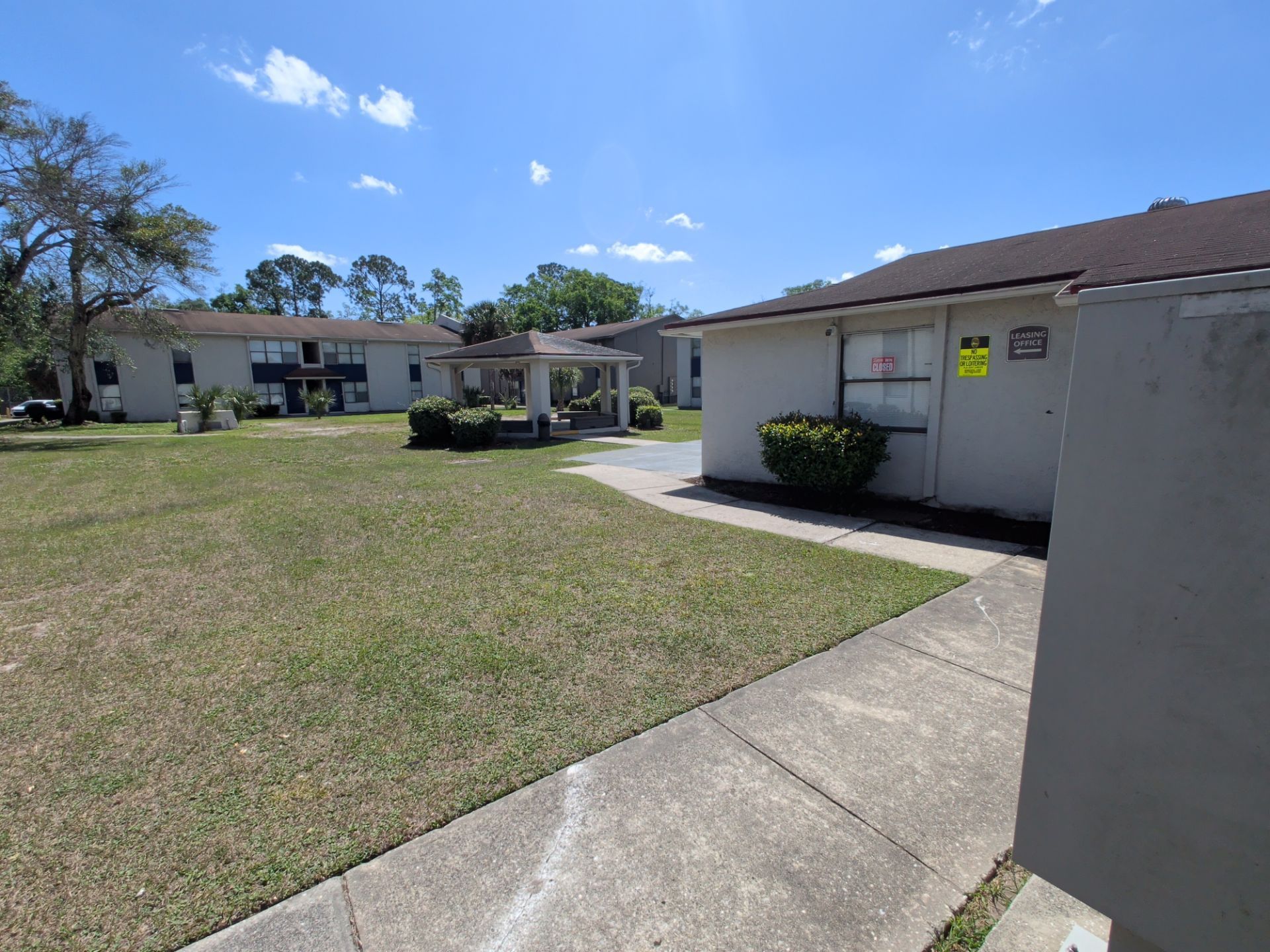 Courtyard with apartment buildings, grassy lawn, and concrete walkway under a sunny blue sky