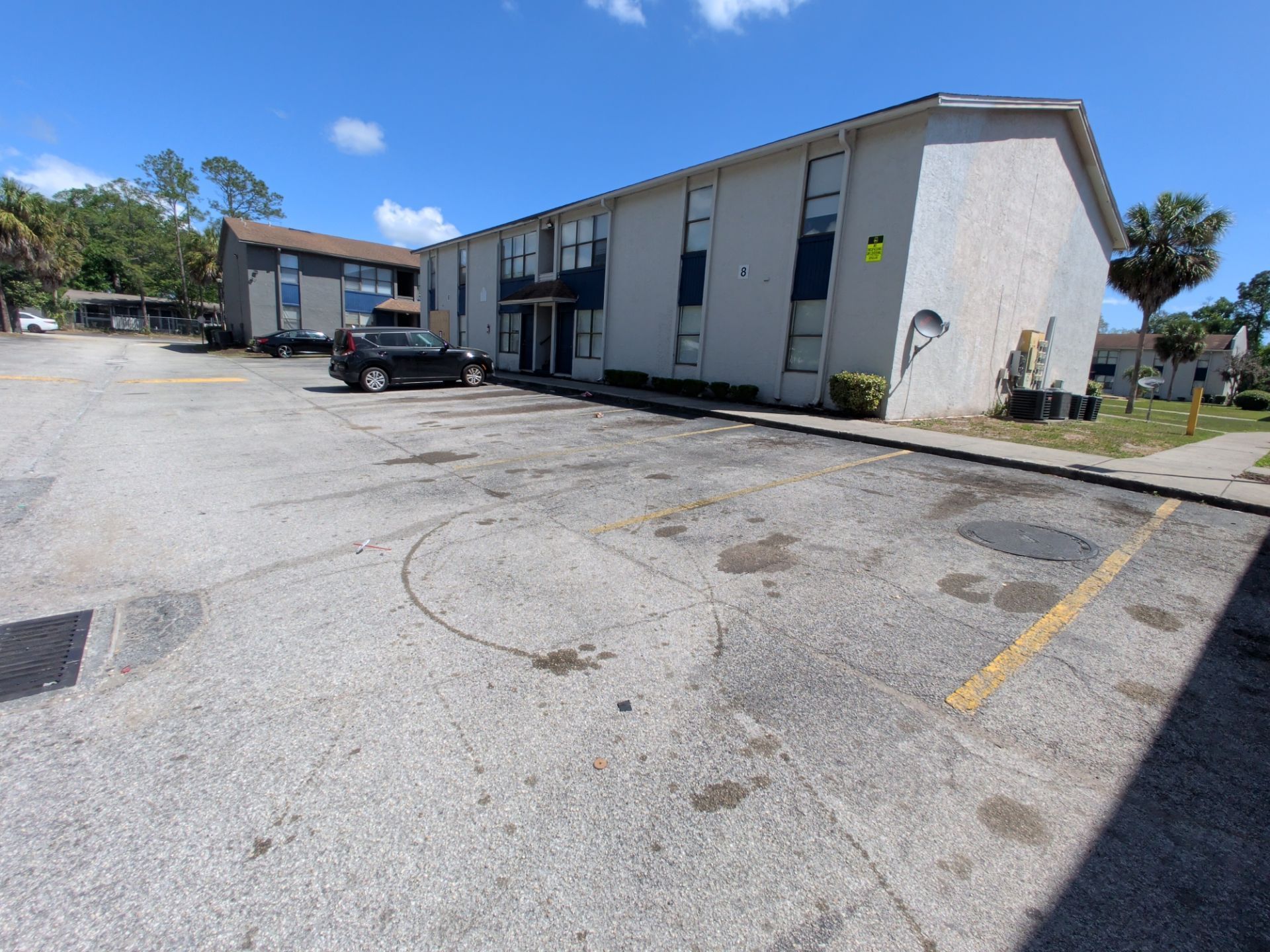 Apartment building parking lot with a parked black car and cracked pavement under a blue sky