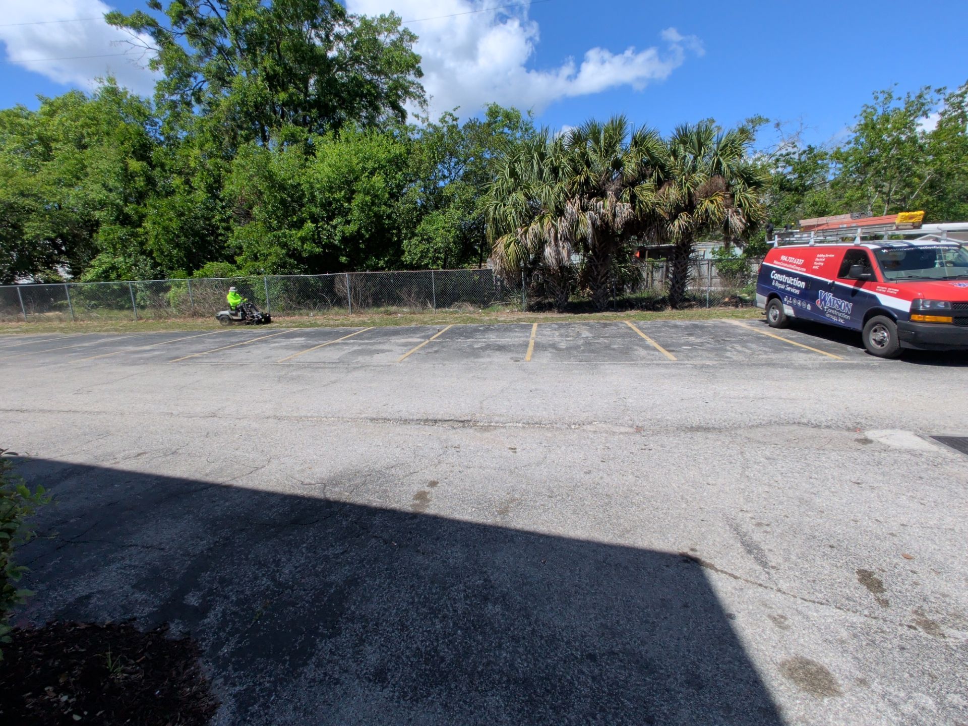 Parking lot with a police vehicle on the right and a motorcycle near a tree line under a blue sky