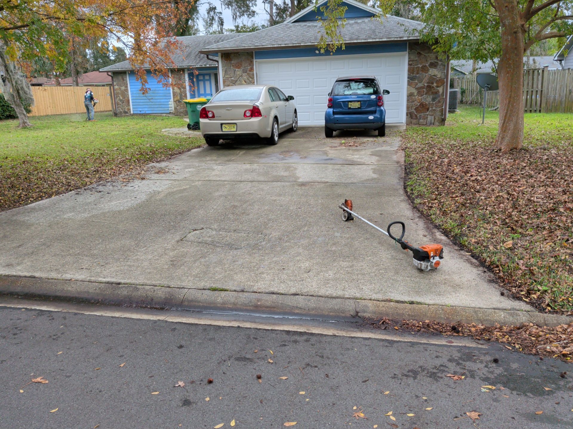 Driveway with cars, a string trimmer, and a house with a garage and lawn.