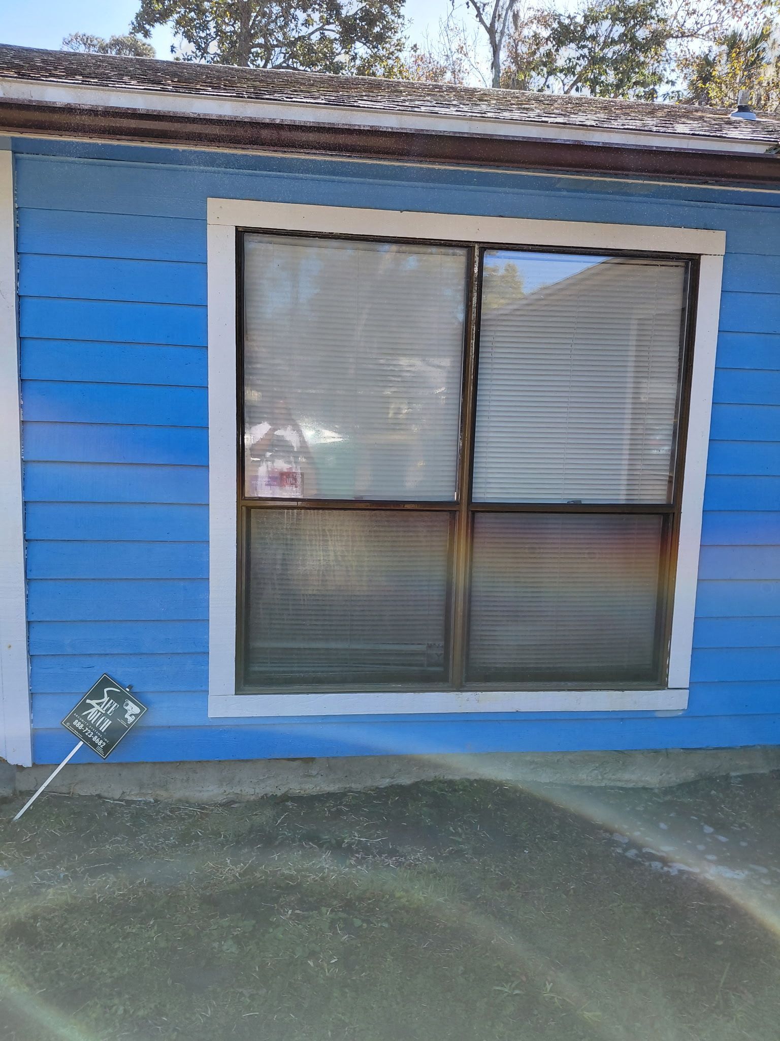 Blue house exterior with a window; white trim, blinds, and a small sign visible.