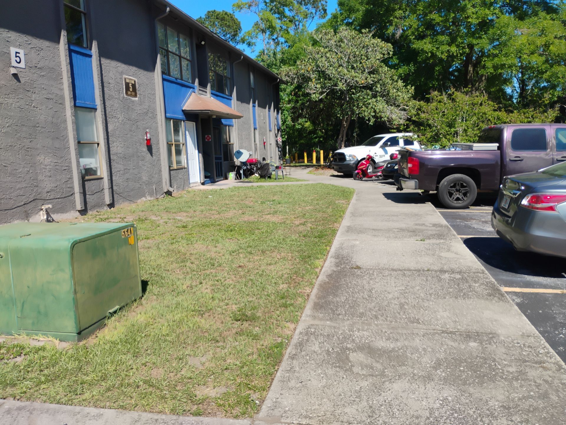 Apartment building with parking lot, concrete walkway, and parked cars on a sunny day