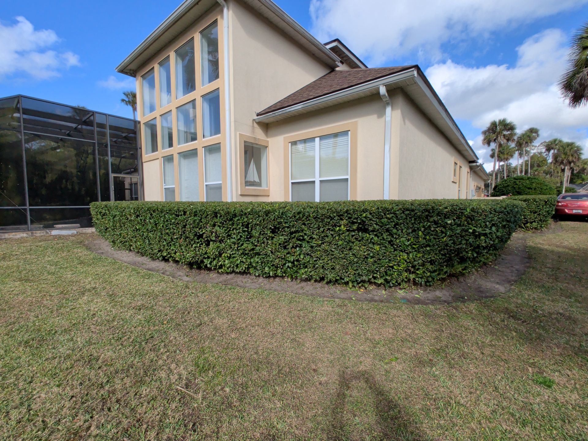 Tan house with trimmed green hedges and lawn under a blue sky.