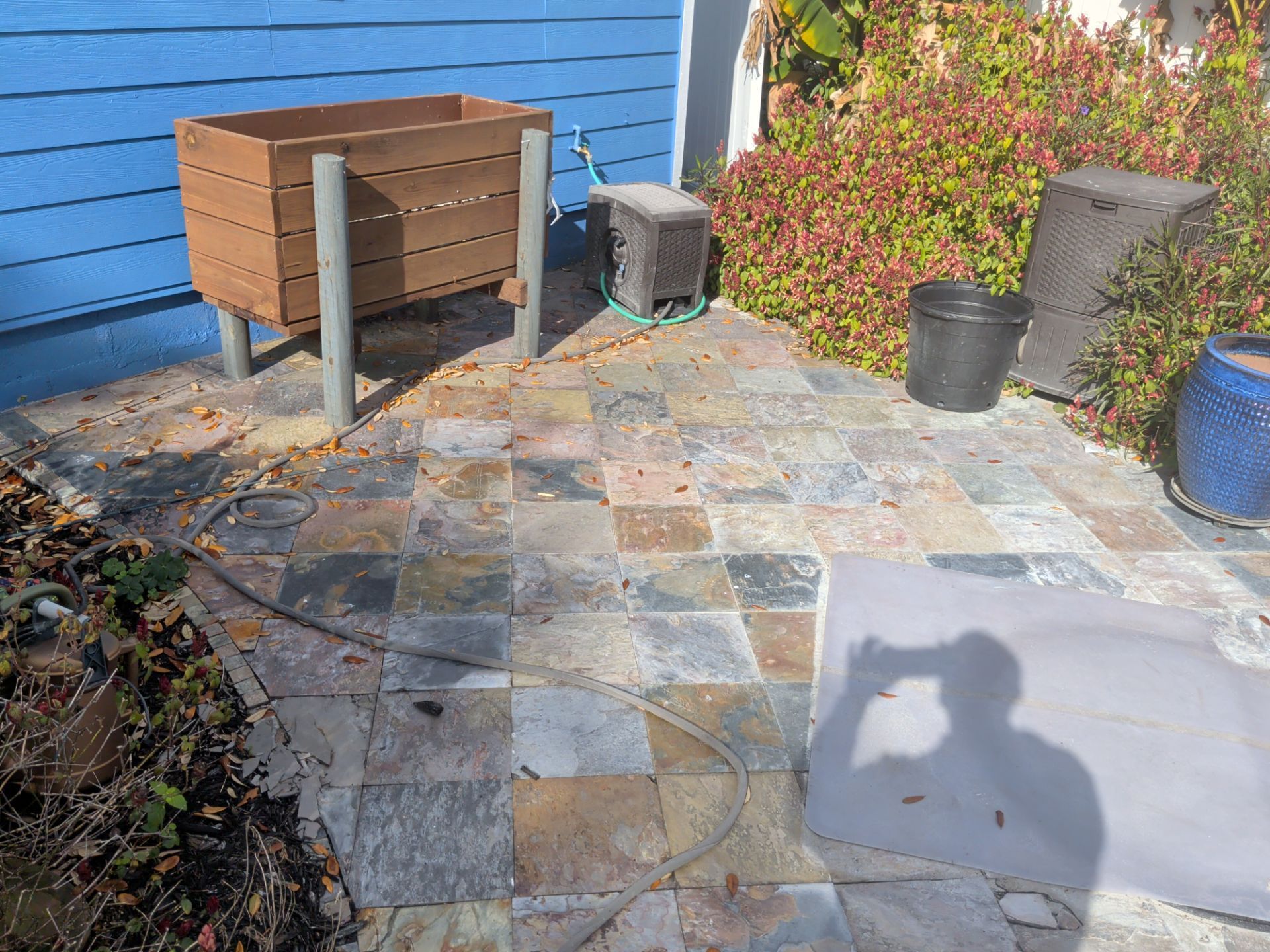 Patio with slate tiles, wooden planter box on legs, various pots, and a shadow.