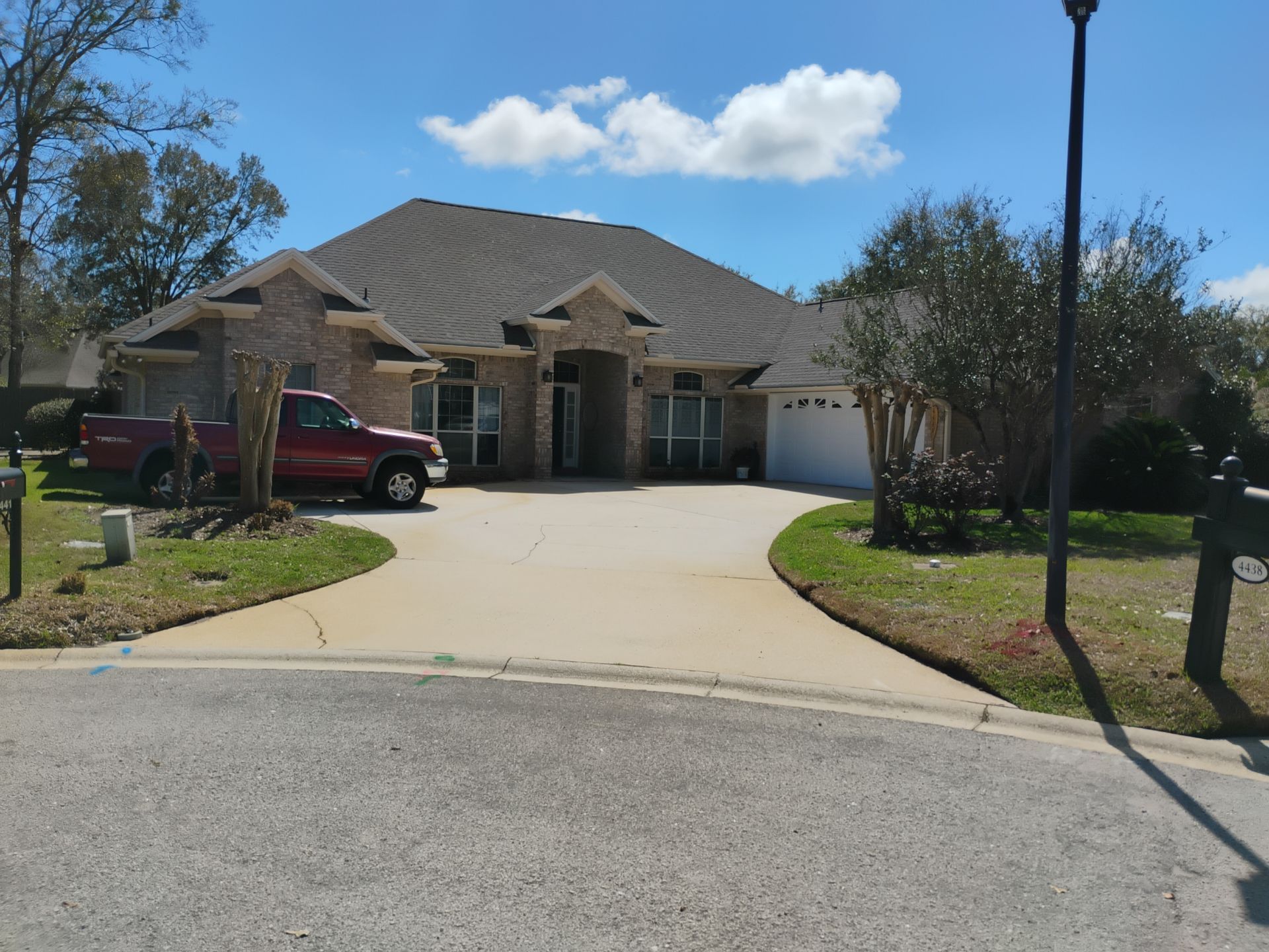 Suburban brick house with a curved driveway, red truck, and blue sky on a sunny day