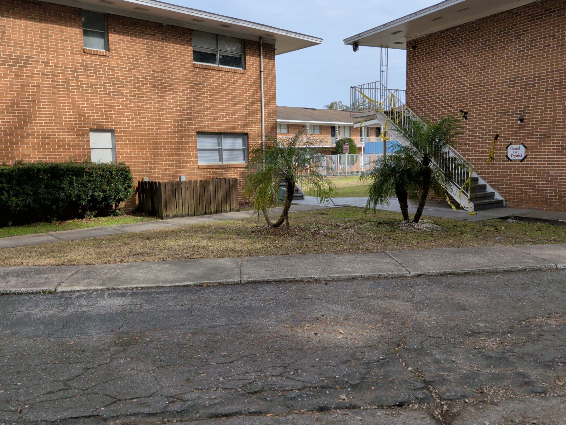 Two brick apartment buildings with palm trees in front and a small park in the background.