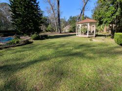 Lush green lawn with a gazebo in a park-like setting. Trees and blue sky visible.
