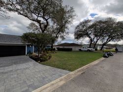 House with blue siding, dark garage door, paved driveway, green lawn, trees, and cloudy sky.