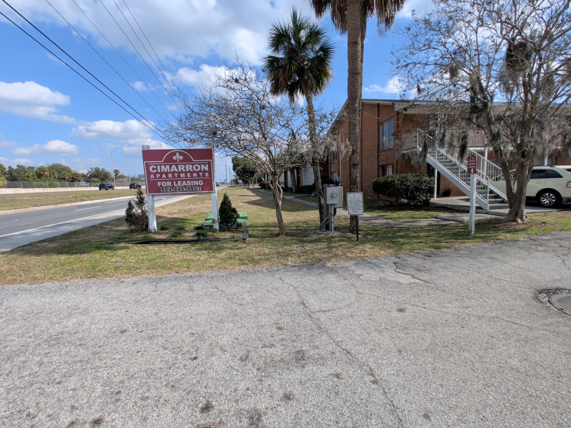 Sign for Allison Apartments next to a road, with a two-story brick building and a palm tree.