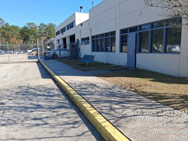 School building with blue windows beside a curb and empty asphalt lot in bright sunlight