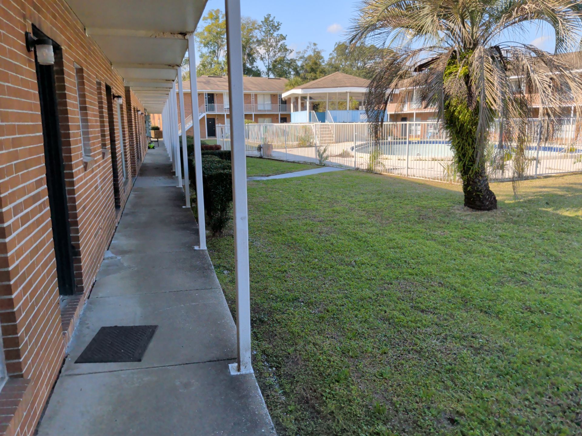 Apartment building hallway with brick exterior, covered walkway, and grassy yard.