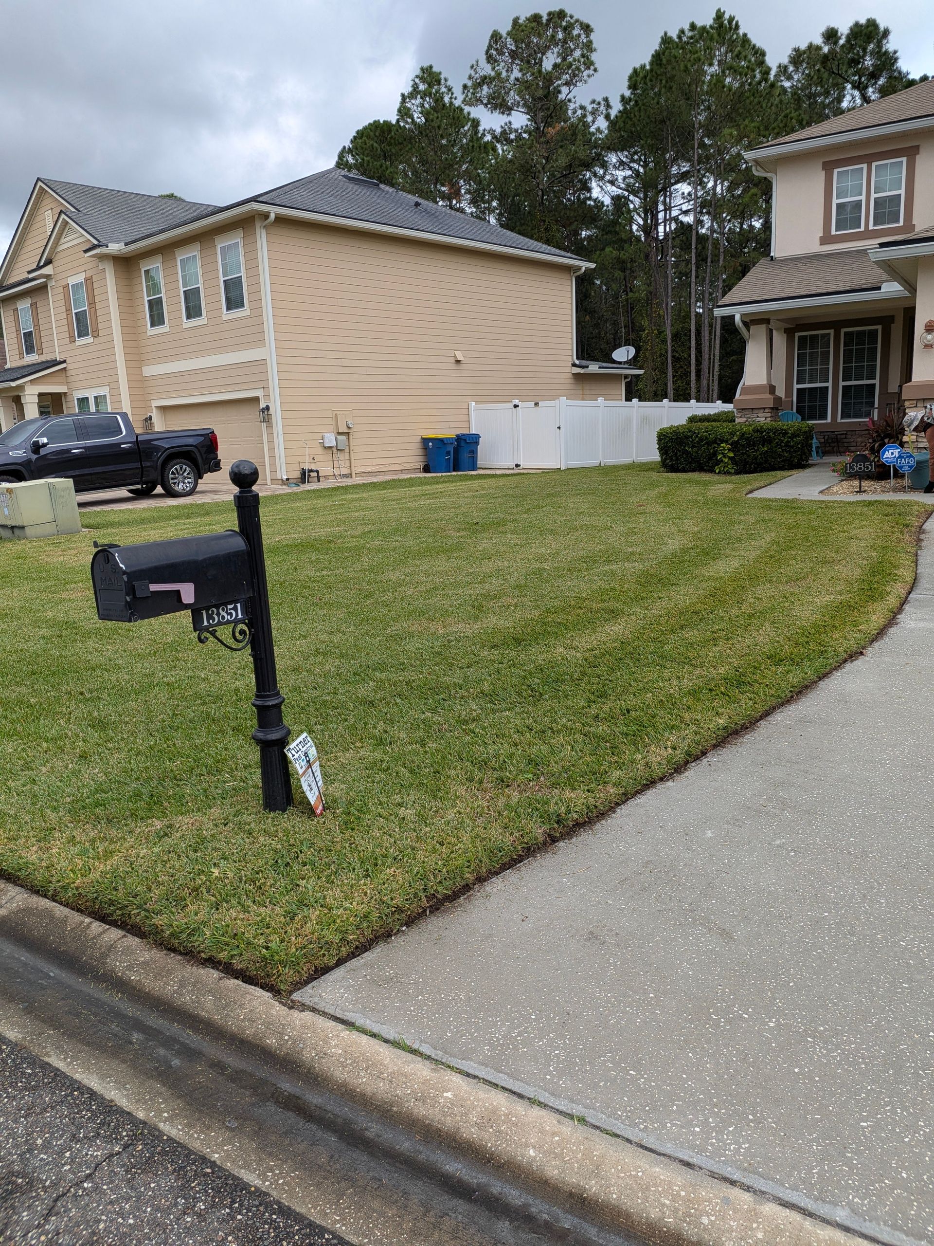 Suburban house exterior with a green lawn, mailbox, driveway, and trees in the background