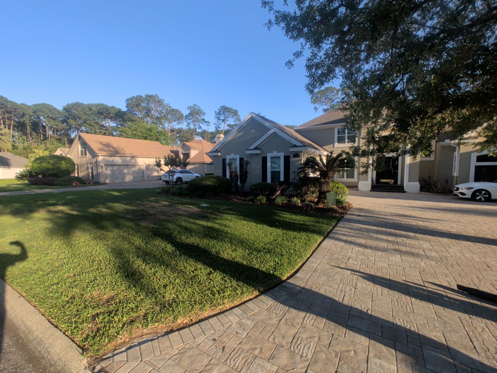 Sunny suburban driveway beside a white house with a manicured lawn and parked car