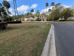 Grassy lawn and road curve towards houses, under a blue sky with clouds.