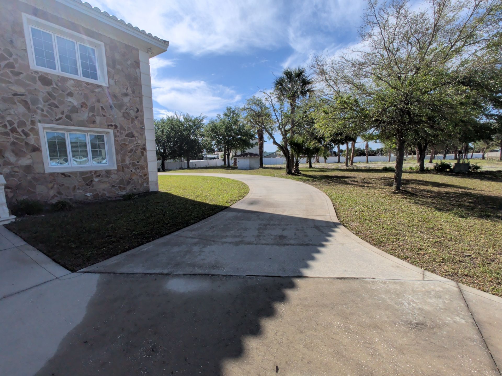 Curved sidewalk beside a stone building in a sunny park with trees and water in the distance