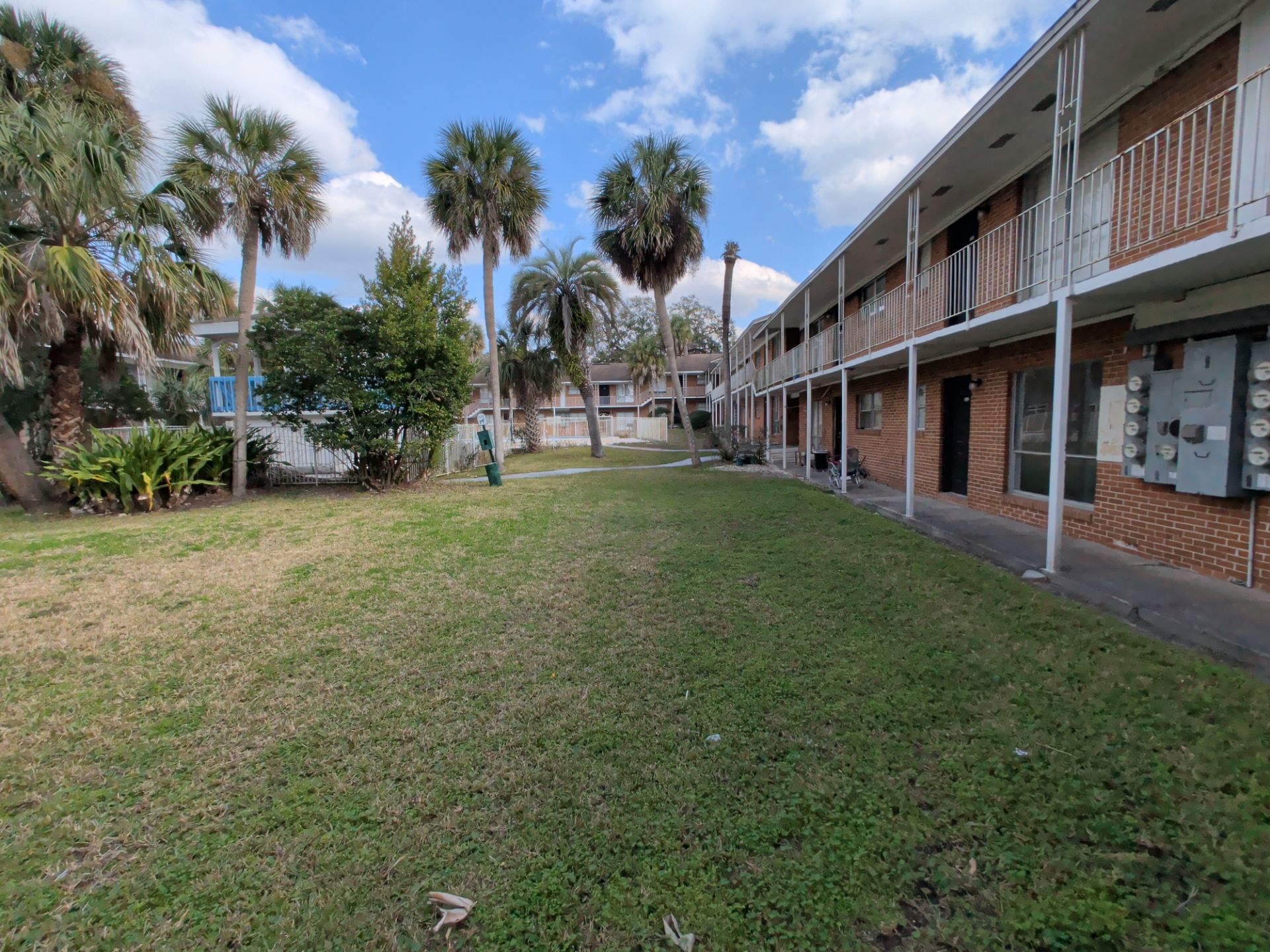 A grassy area between a two-story apartment building and trees under a blue sky.