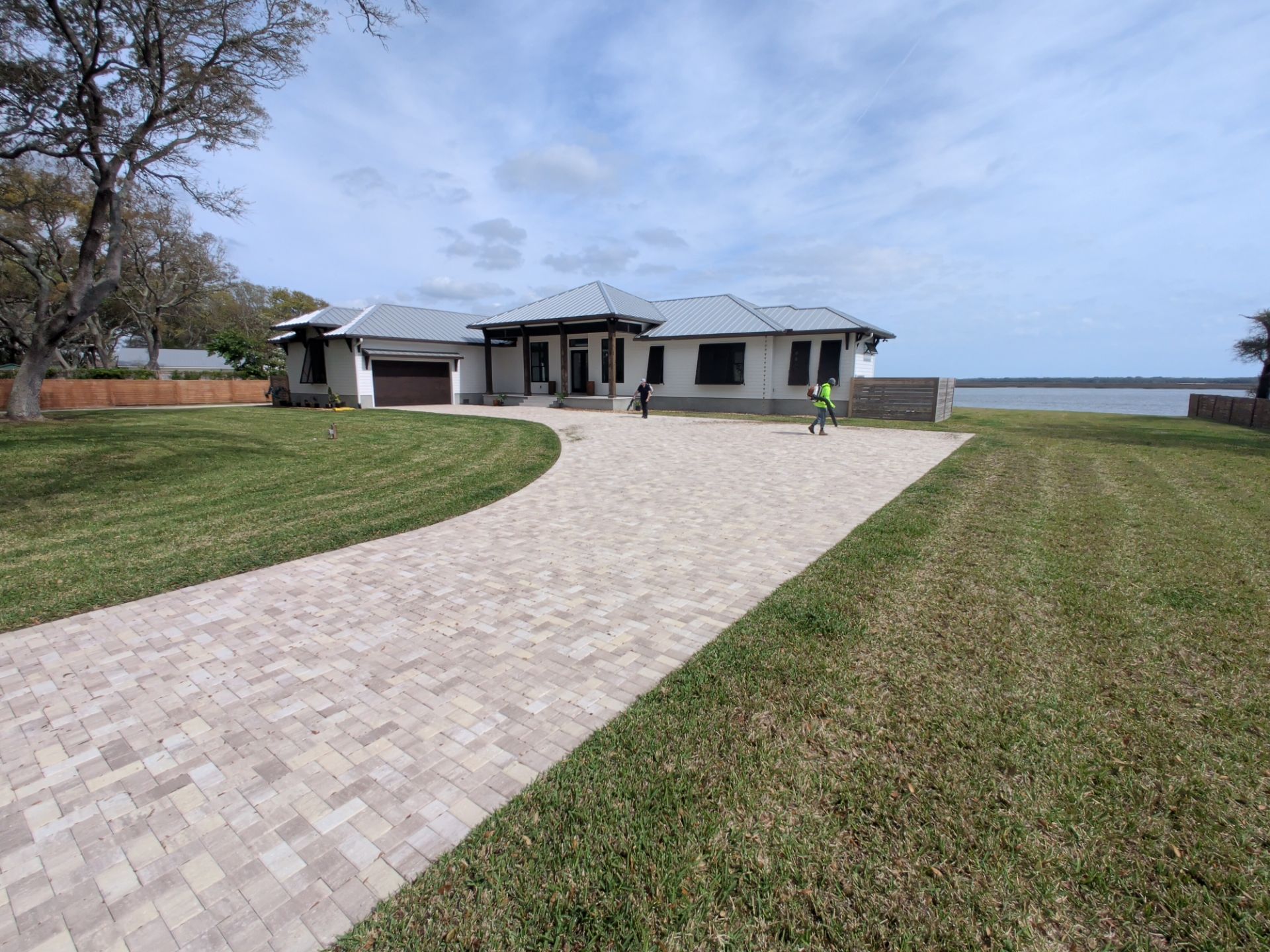 Single-story house with curved brick driveway, manicured lawn, and waterfront view