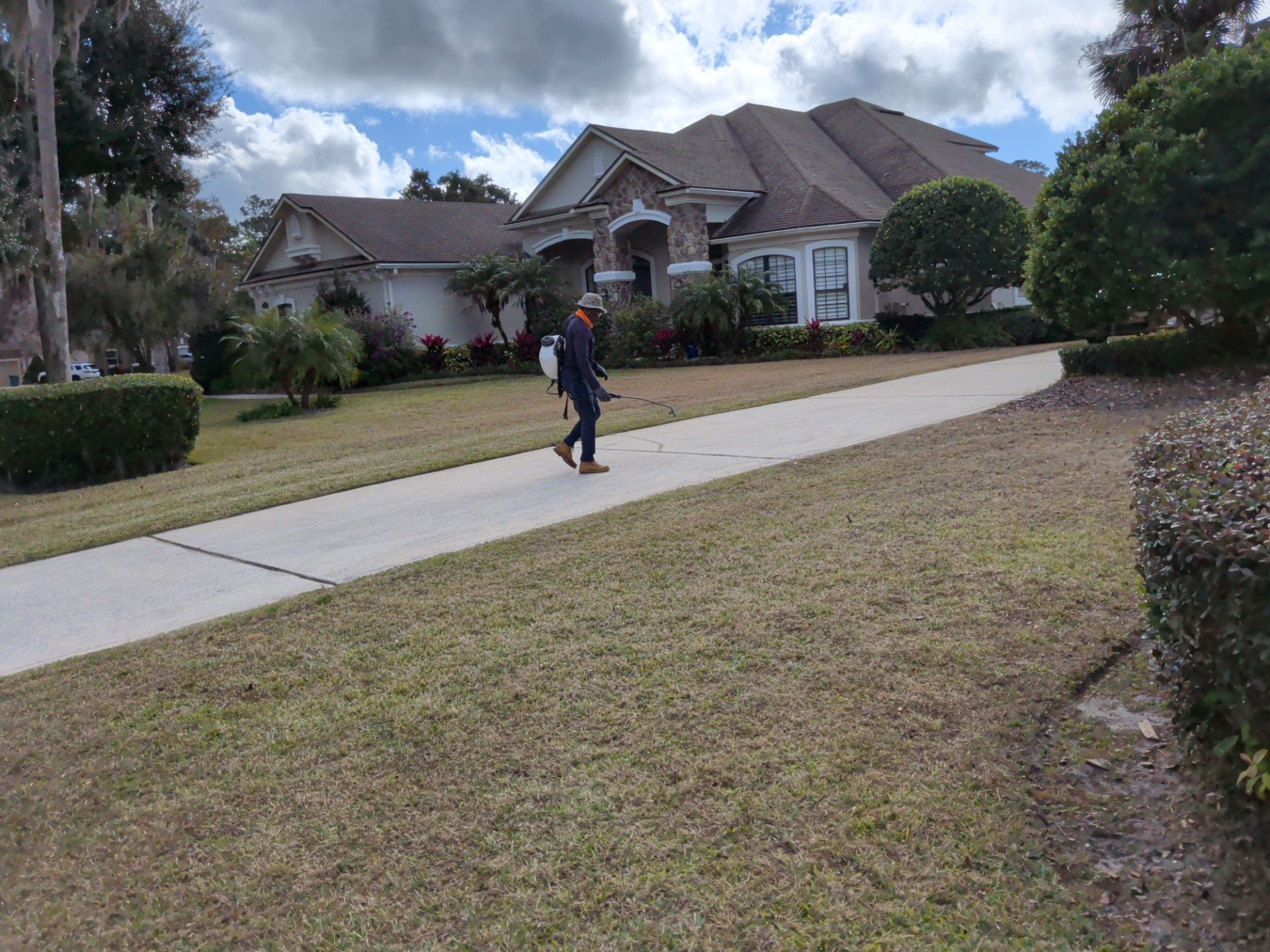 Person walking on a driveway toward a large suburban house on a cloudy day