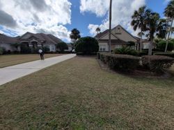 A person walks down a sidewalk in front of two houses with brown roofs on a sunny day.