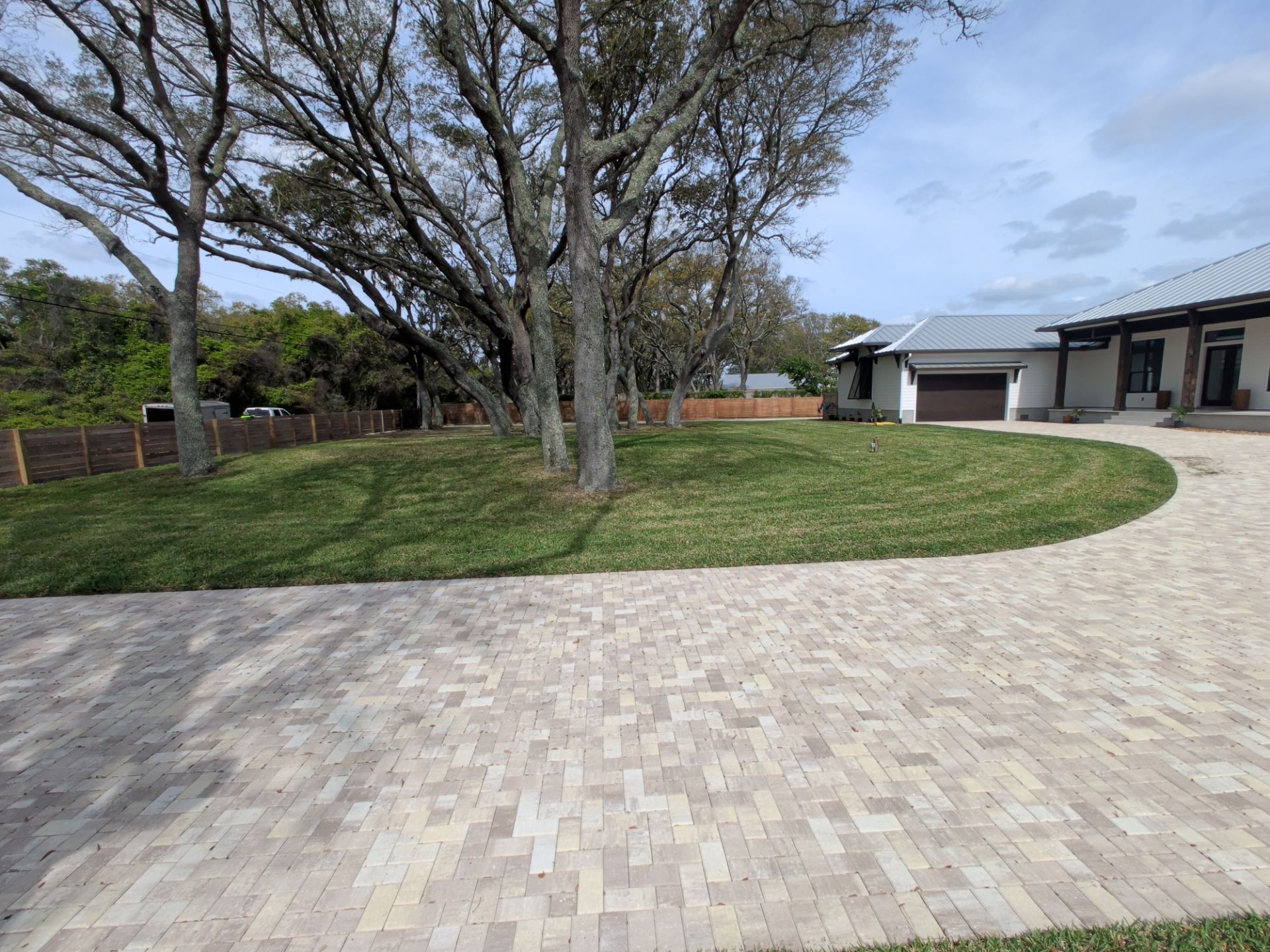 Paved courtyard beside a grassy lawn and trees, with buildings lining the right side.