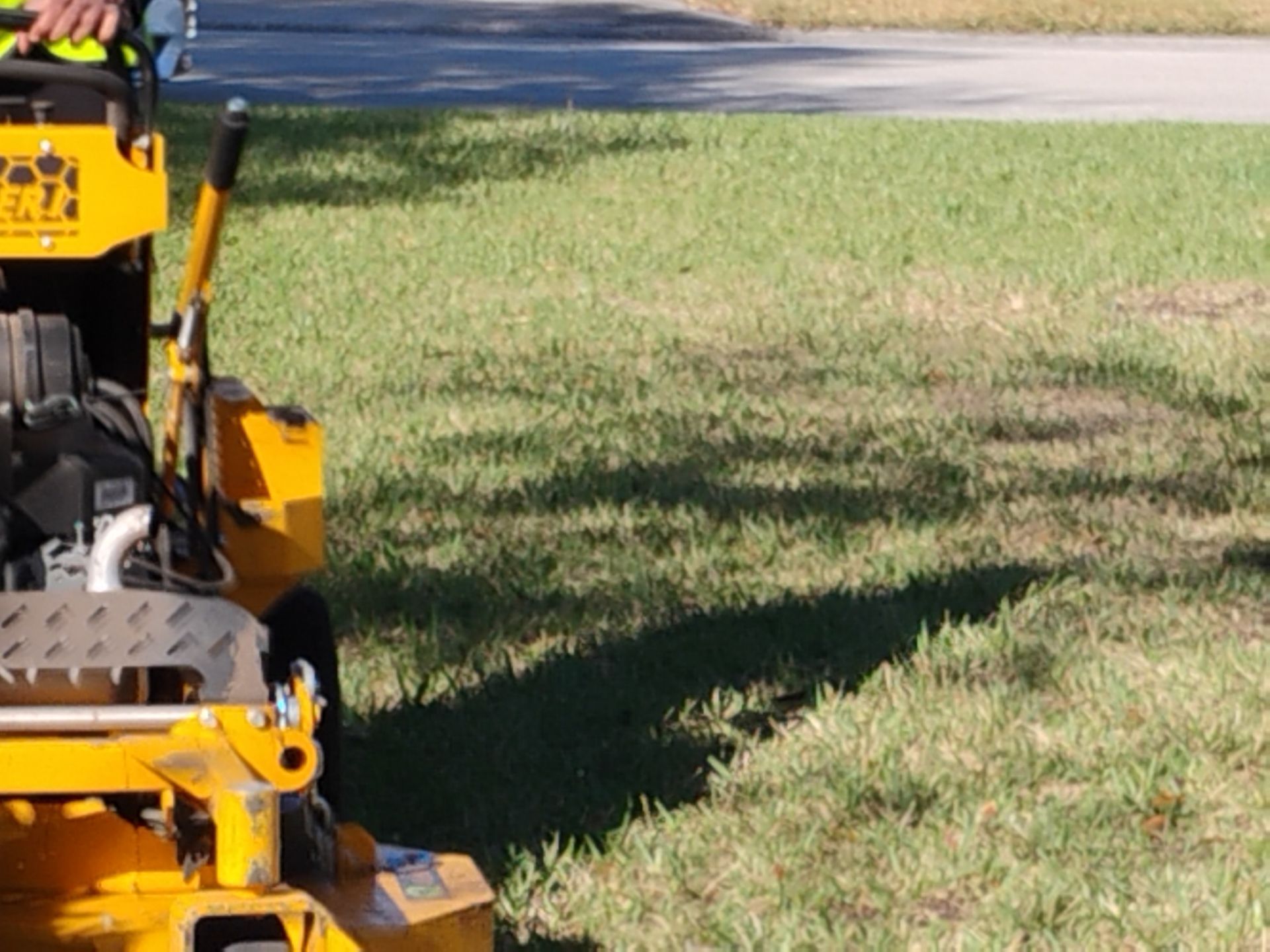 Yellow lawn mower cutting grass beside a road on a sunny day