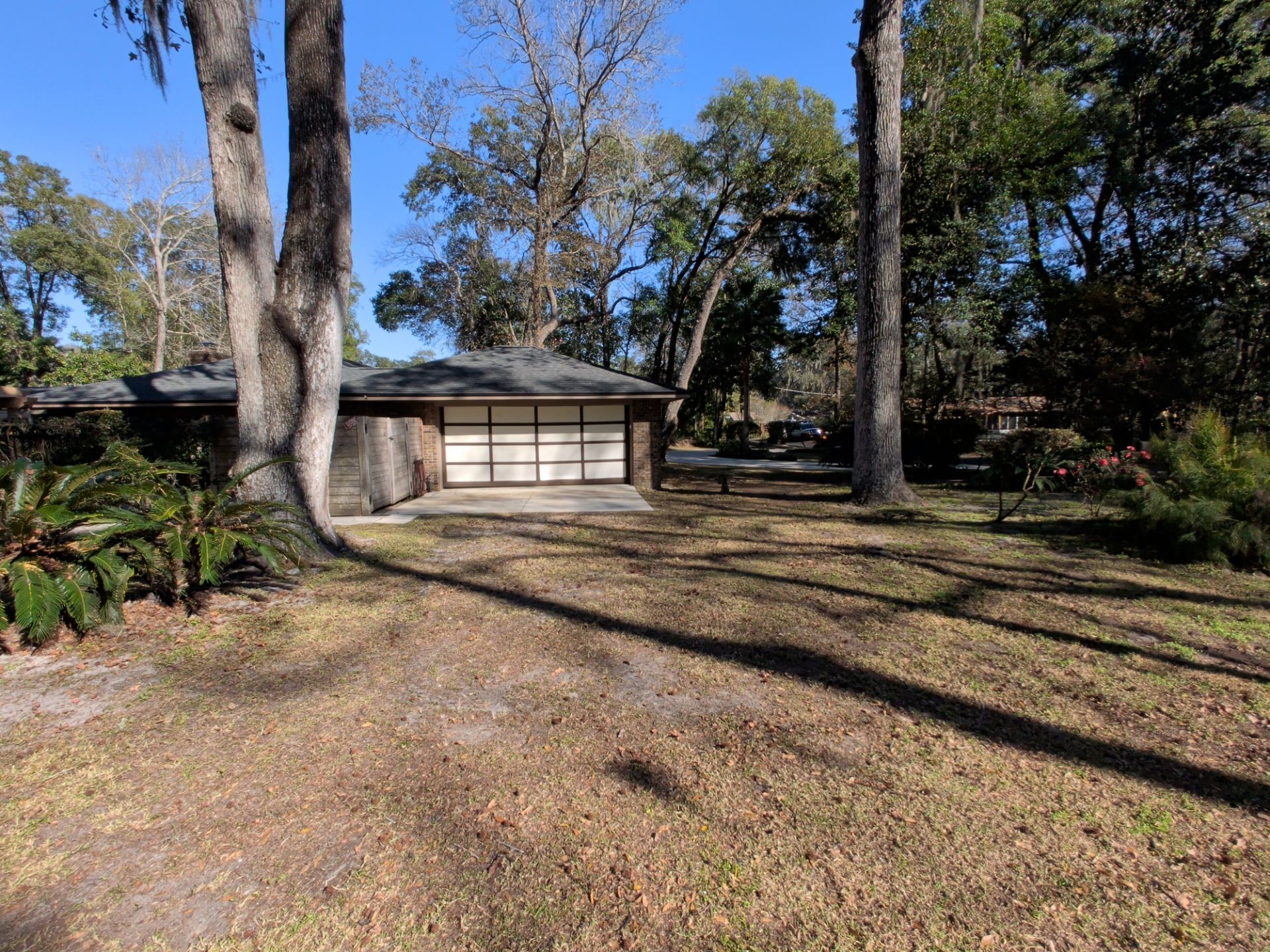 Garage with white doors on a sunny day, surrounded by trees and a brown yard.