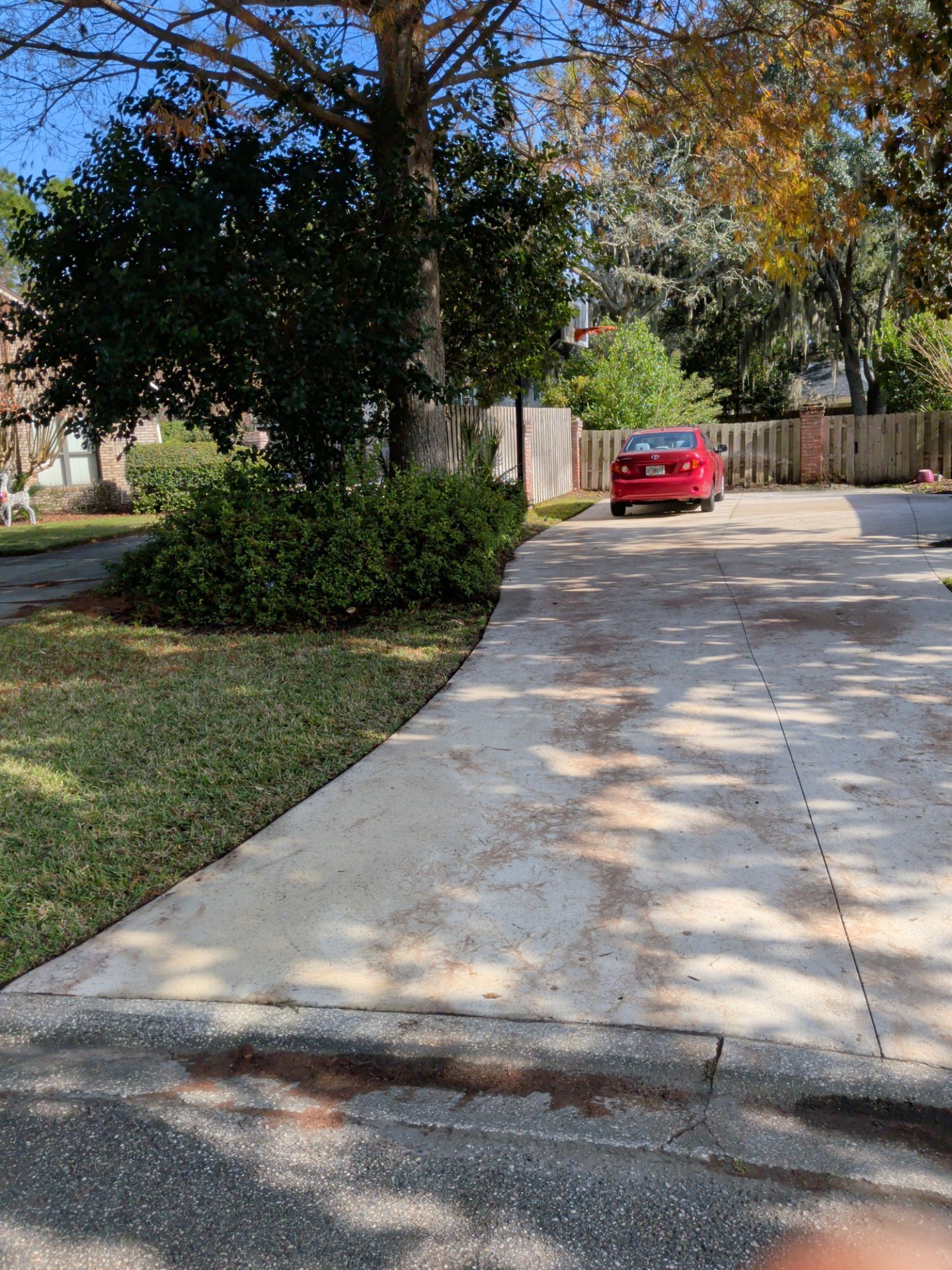 Driveway leading to a red car parked near a wooden fence under trees with autumn leaves.