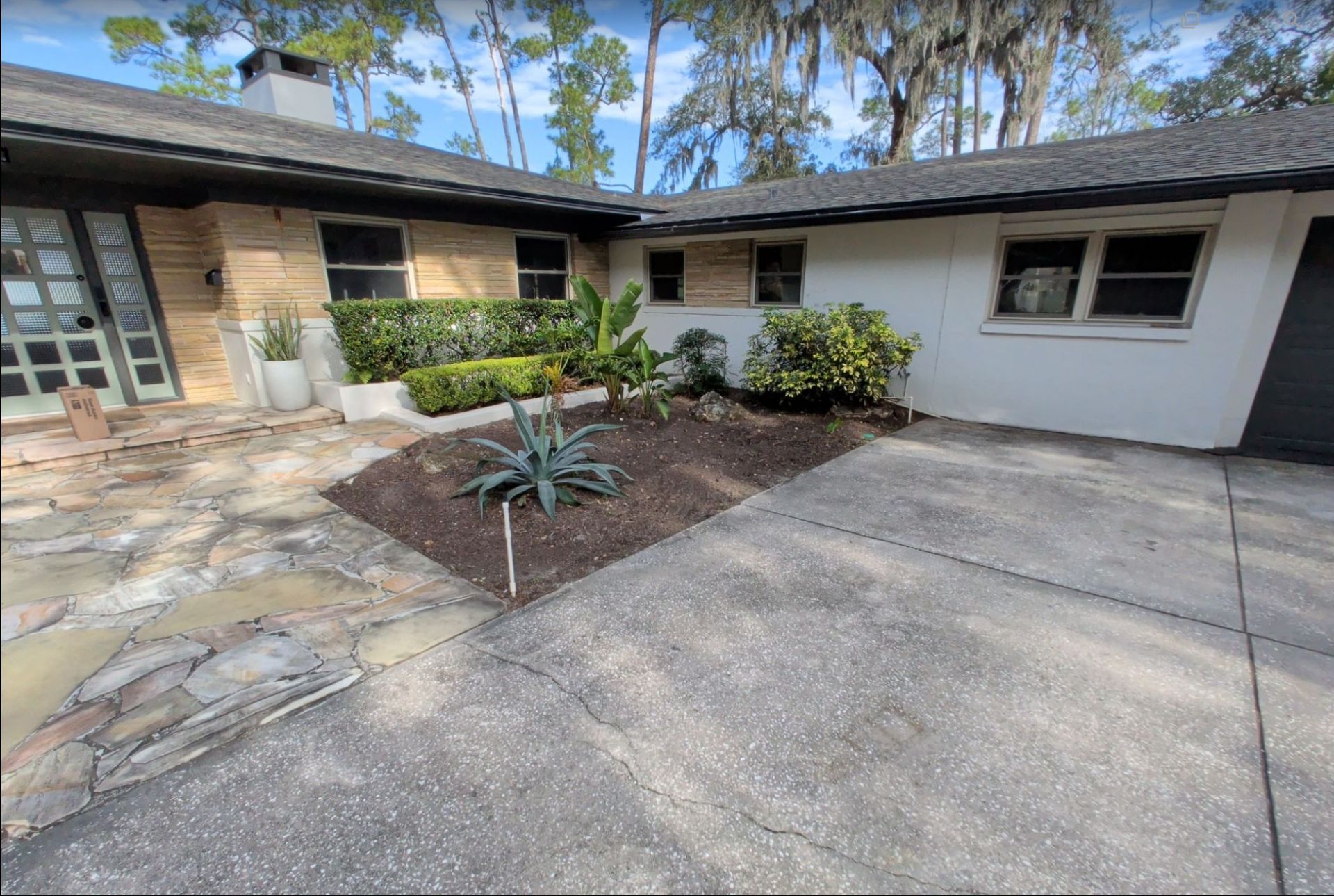 Courtyard with stone walkway, concrete driveway, and small landscaped bed in front of a single-story house