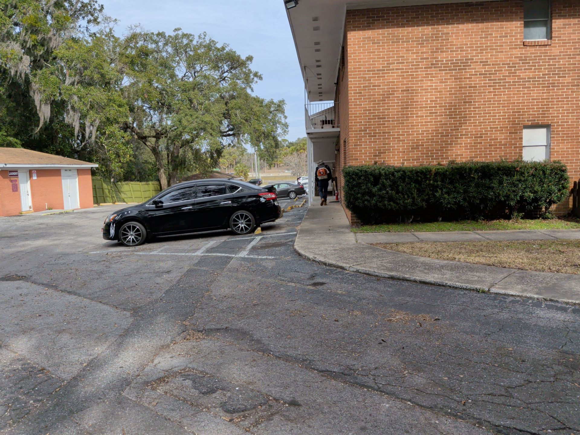 Black car parked near a brick building and small shed on a sunny day.