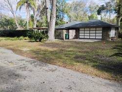 House with a dark roof and a garage, on a grassy lot, trees in the background.