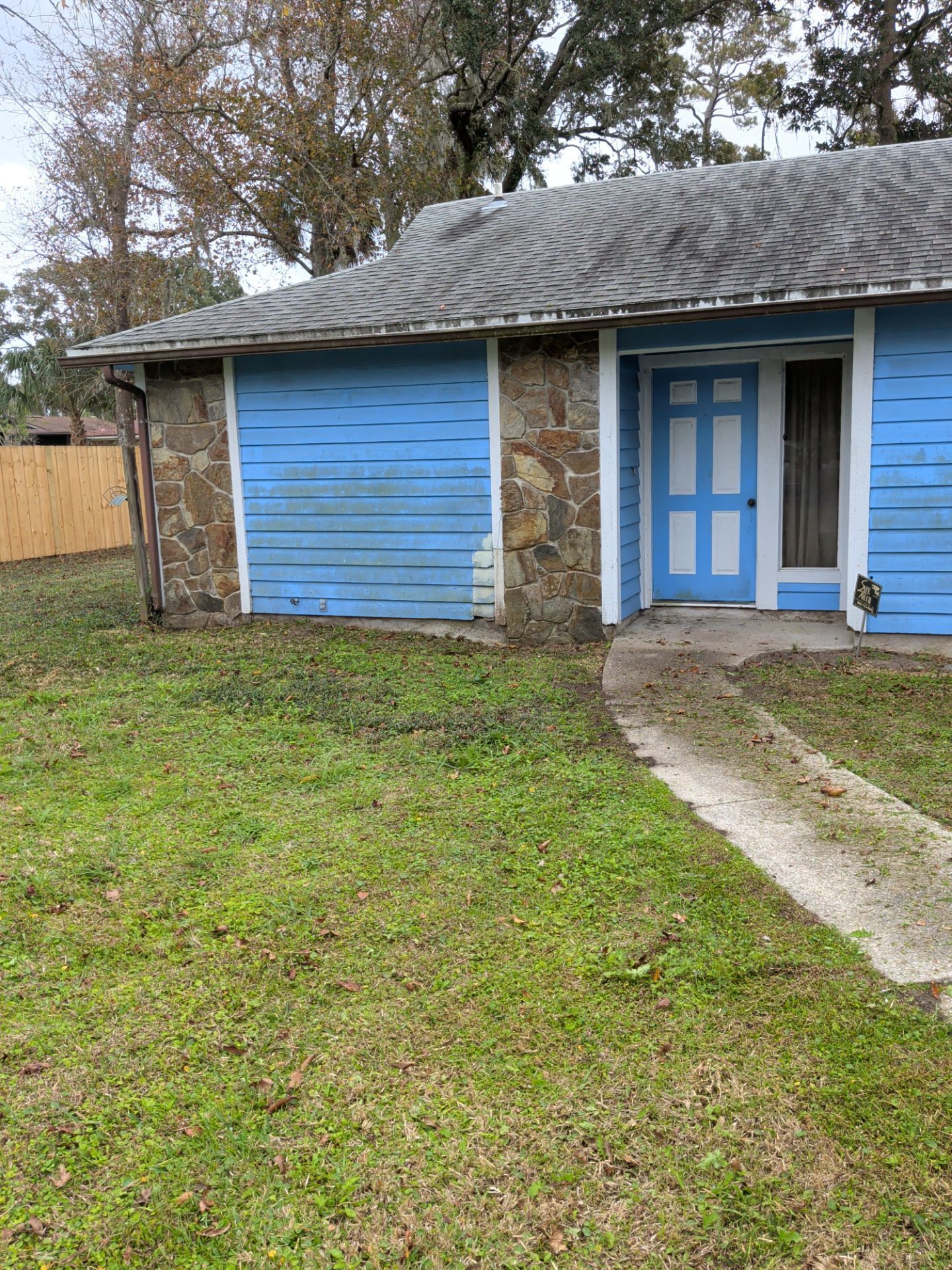 Blue house with stone accent, a blue garage door, a white door, and a concrete walkway.
