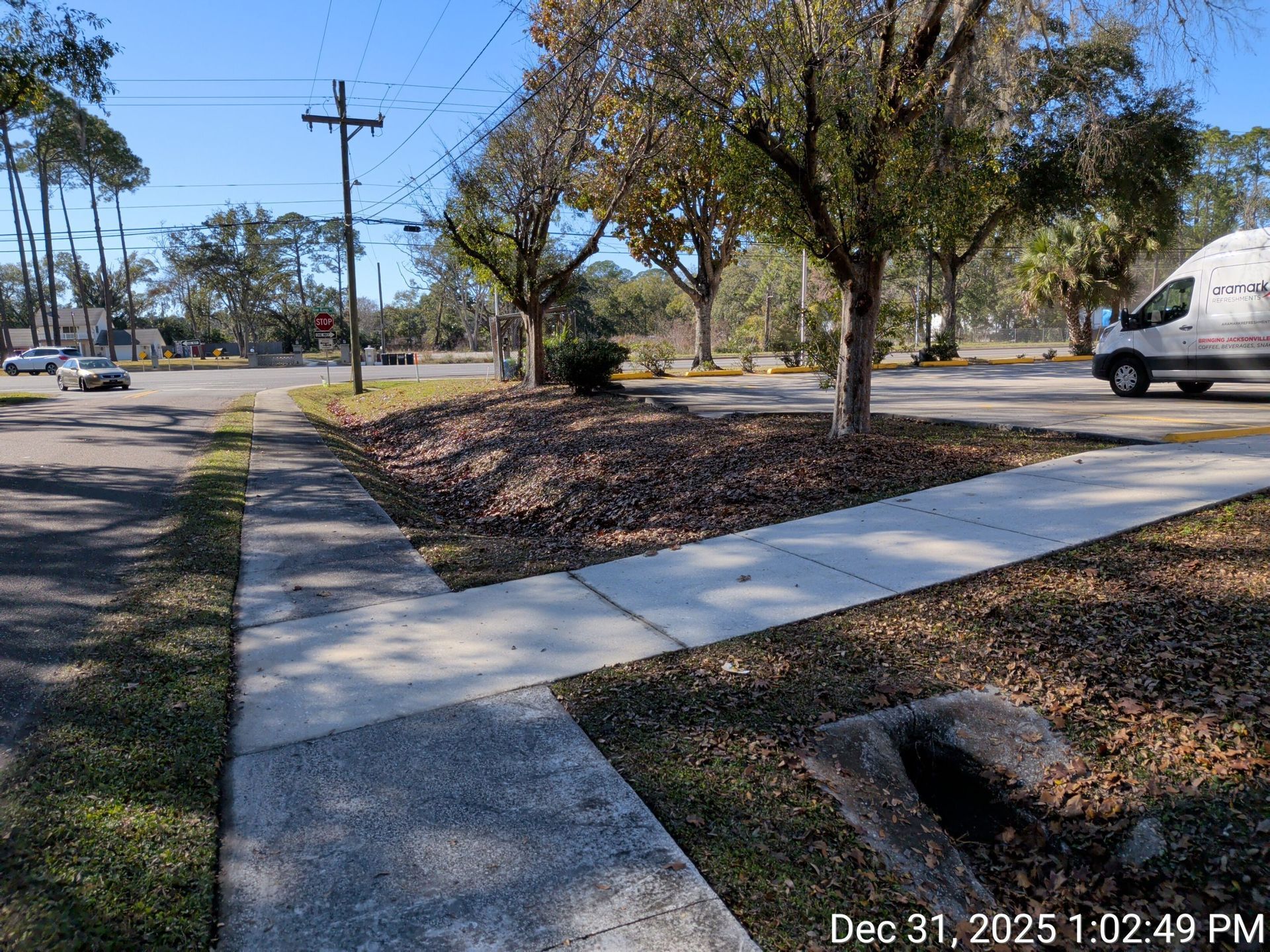 Sidewalk leading to a road intersection with trees and a utility pole on a sunny day.