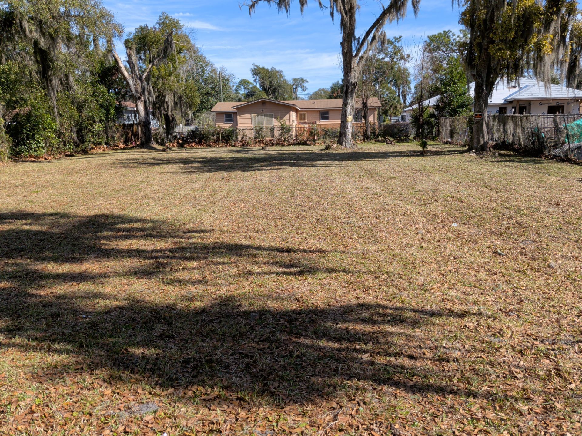 Cleared lot with brown grass, trees in background, and houses visible.