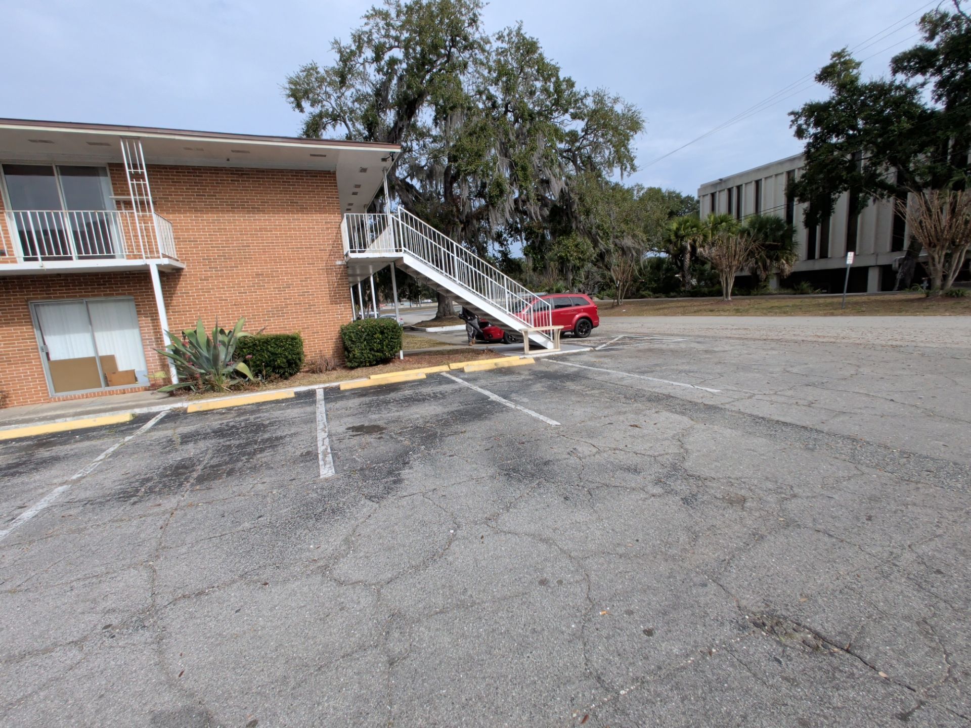 Apartment building with exterior stairs and parking lot on a cloudy day. Red car parked near stairs.