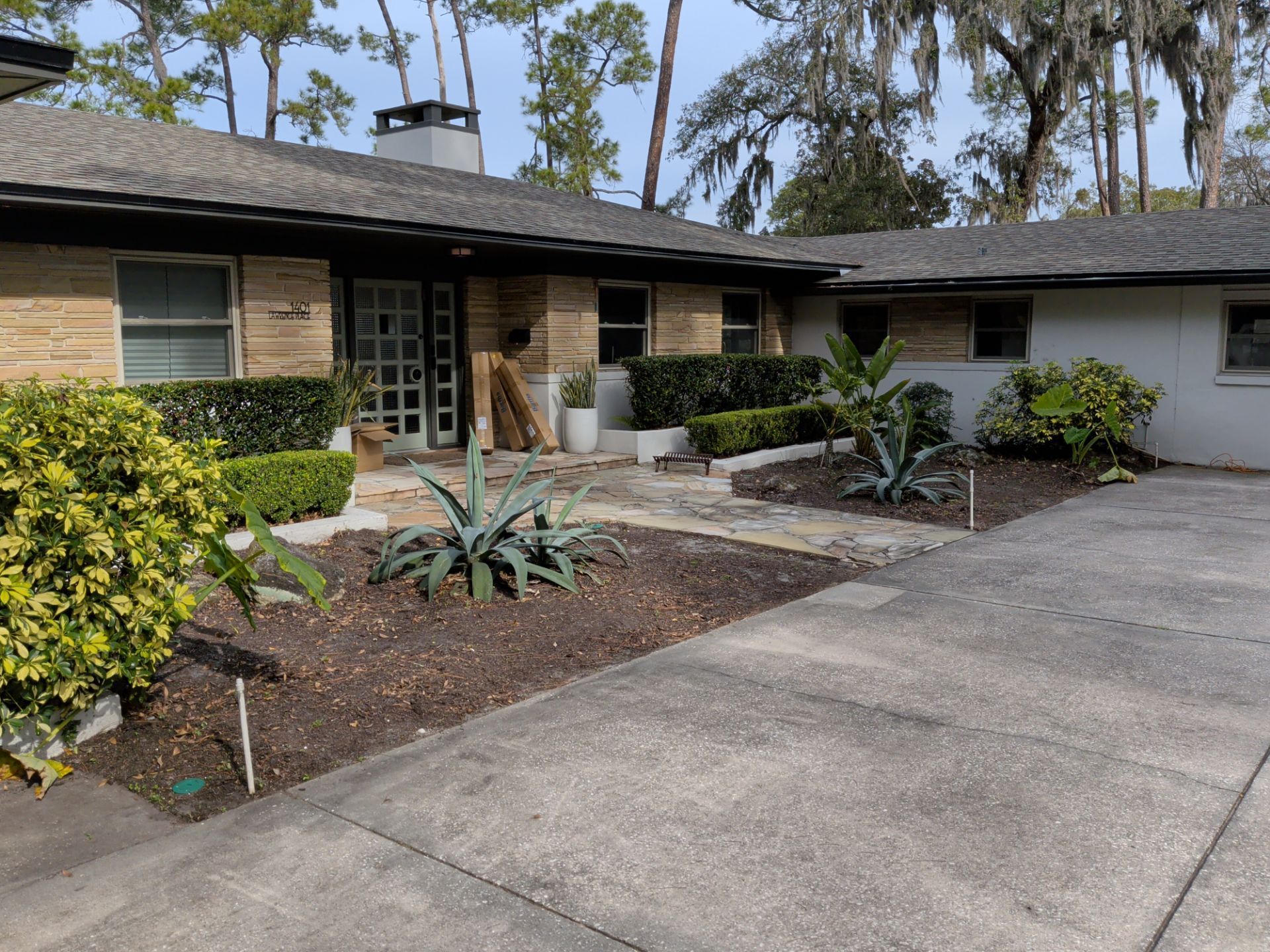 A single-story brick house with a concrete driveway and landscaped yard with shrubs and agave plants.