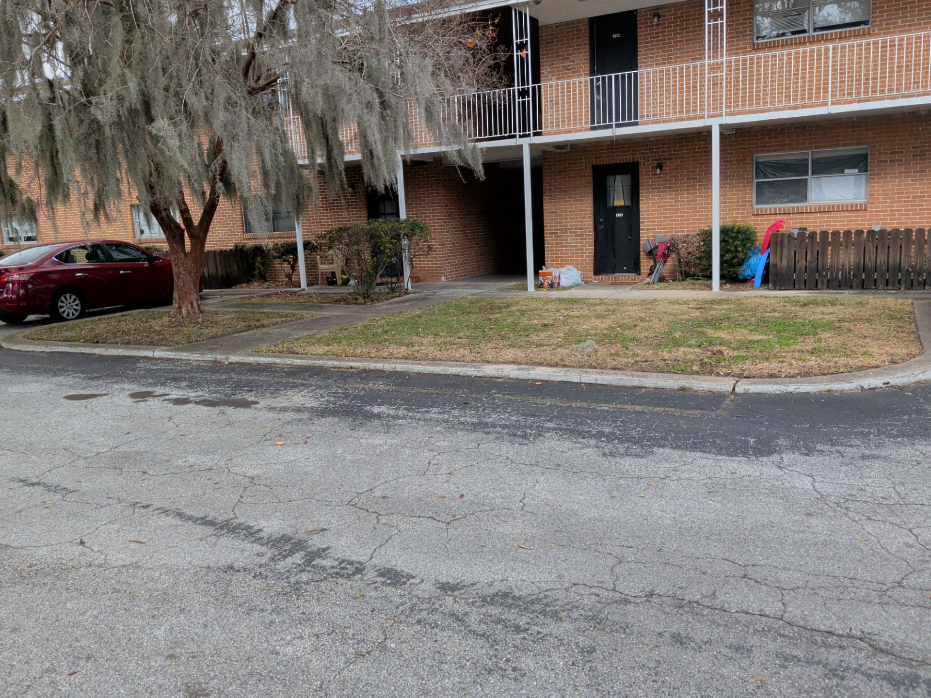 Apartment building with a red car parked nearby. A tree with hanging moss is in the foreground.