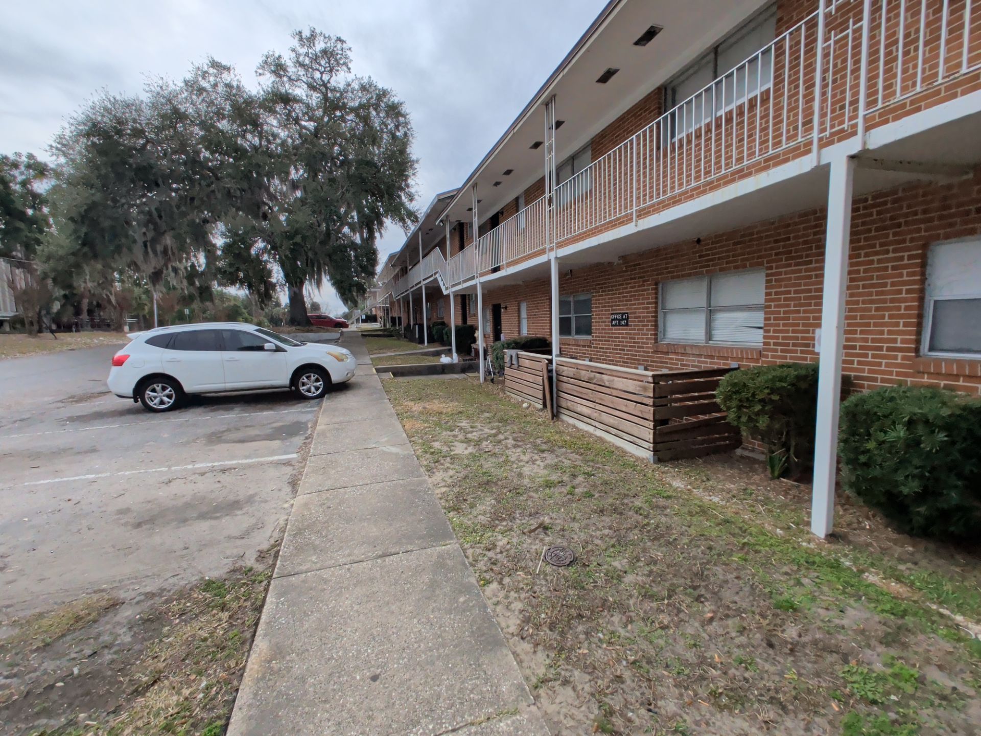 Apartment building with a sidewalk, parked white car, and overcast sky.