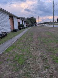 Apartment building exterior, sidewalk, and grassy area under a cloudy sky.