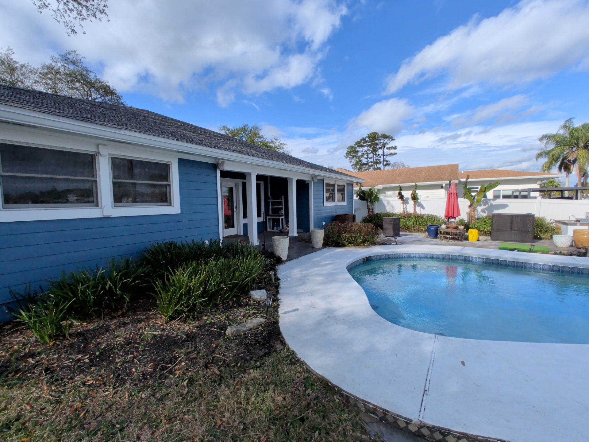 Blue house with a pool in backyard on a sunny day.