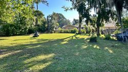 Lawn mower cutting grass in a sunny yard with trees and a house in the background.