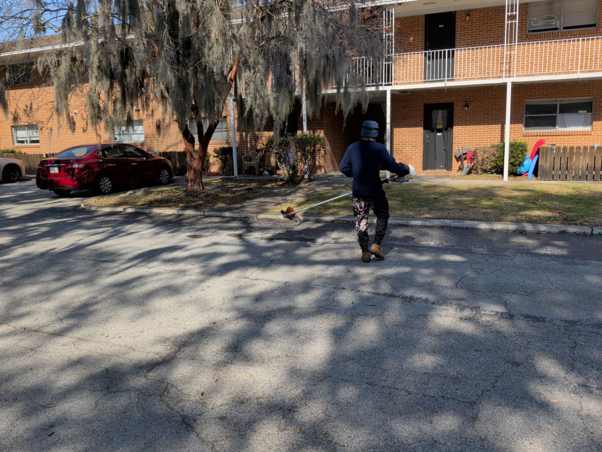 Person riding a scooter in a paved area, trees and a brick apartment building in the background.