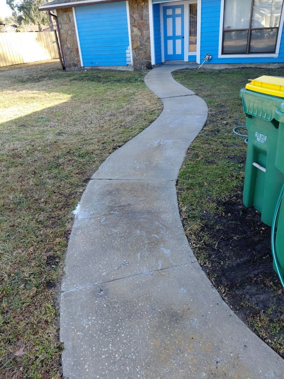 Curving concrete sidewalk leading to a blue house with a matching door. A green trash can is on the right.