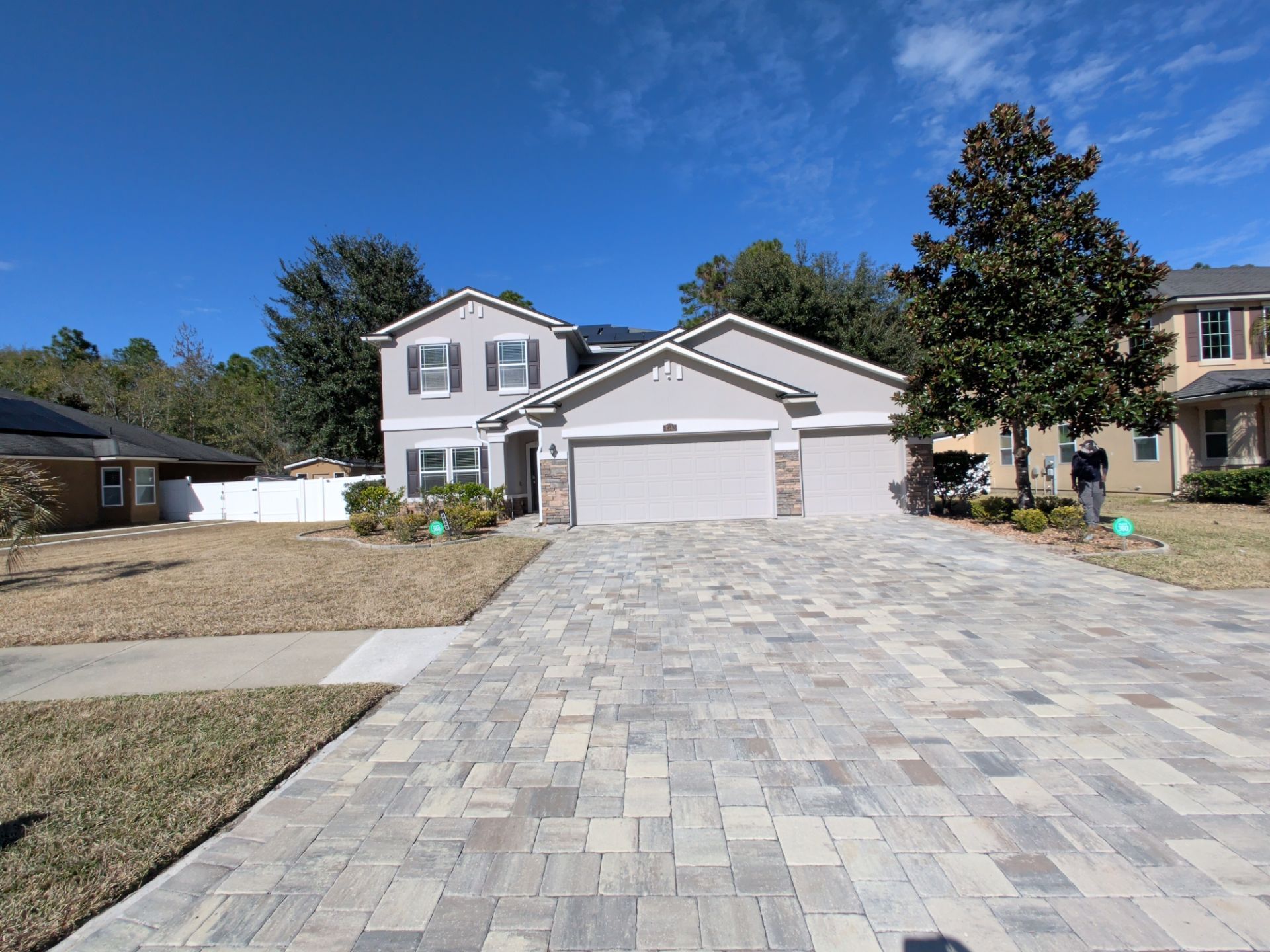 Two-story house with gray facade, two-car garage, and patterned brick driveway under a blue sky.