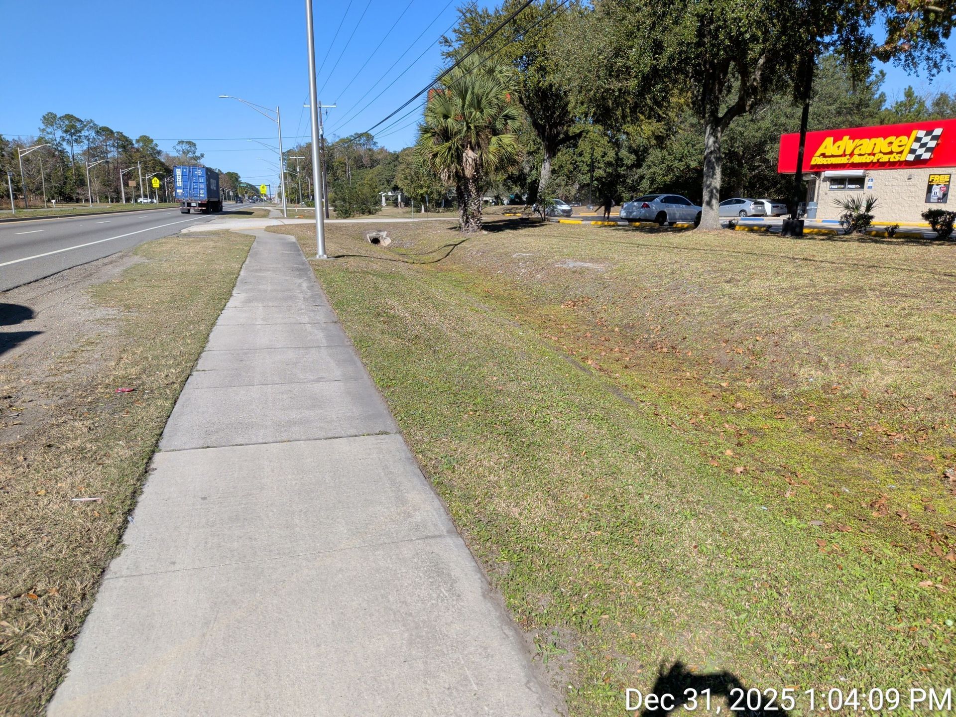 Sidewalk next to a road, with a partially visible Advance Auto Parts store.